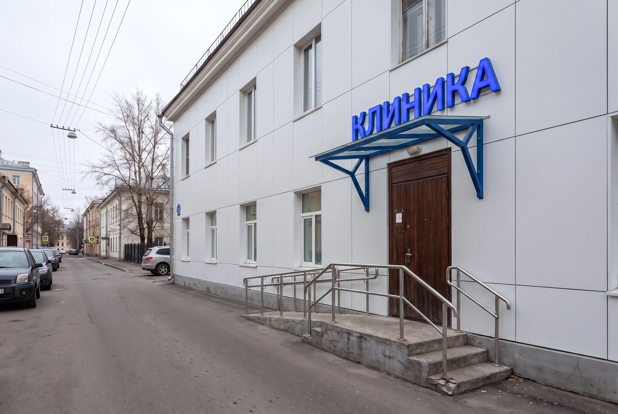 Та же клиника после AI-рендера: белые HPL-панели вентфасада, вывеска КЛИНИКА с LED-подсветкой, пандус и козырёк над входной группой